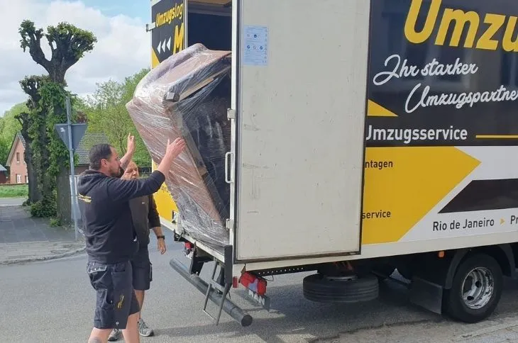 zwei umzugshelfer laden grosses verpacktes moebel in umzugswagen